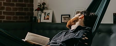 Man resting in a hammock with an open book