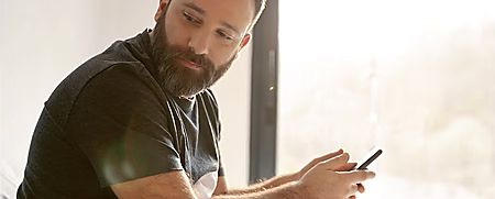 Man sitting by a bright window, looking at his phone